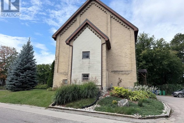 Rear side exterior of a multi-unit brick building with a gabled roof and white siding detail. - Unit 5 - 108 Queen Street N, West Grey