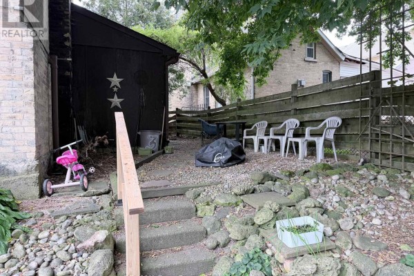 Backyard patio area with gravel, stone landscaping, plastic chairs, and a child's tricycle. - Unit 5 - 108 Queen Street N, West Grey