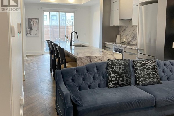Open-concept living area showing a blue sofa, marble island, and modern kitchen. - Unit 5 - 25 Dervock Crescent, Toronto
