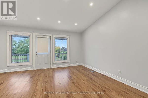 Living room with light wood laminate flooring, white walls, and large windows. - Unit A (upper Unit) - 1135 Maitland Avenue, Ottawa