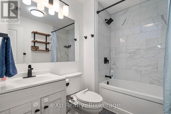 White vanity, toilet, and bathtub with white marble tile surround in the bathroom. - Unit A - 89 College Street E, Belleville