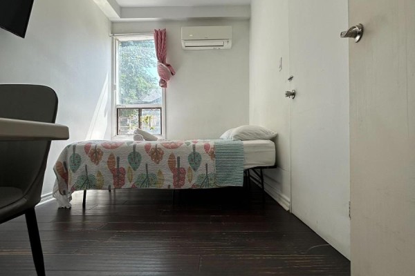 A bedroom with a single bed, white walls, dark wood floor, and a window with pink curtains. - Unit A Main Floor - 3 Pembroke St Street, Toronto