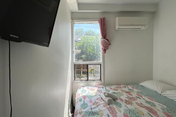 A bedroom with a bed, a mounted flat-screen TV on the wall, and white walls. - Unit A Main Floor - 3 Pembroke St Street, Toronto