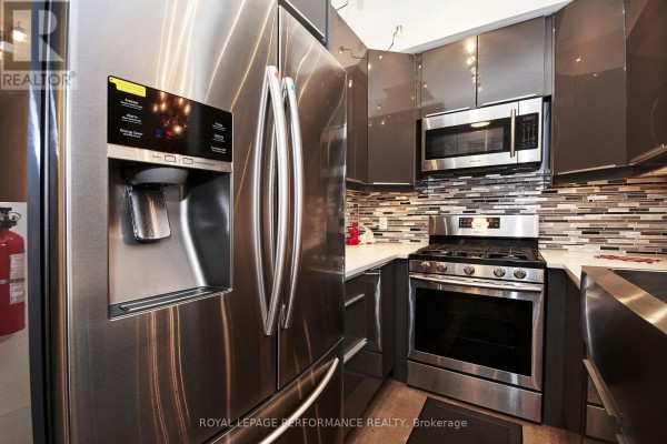 A stainless steel refrigerator and a gas stove are in the compact kitchen with grey cabinets. - Unit B - 82 Third Avenue, Ottawa