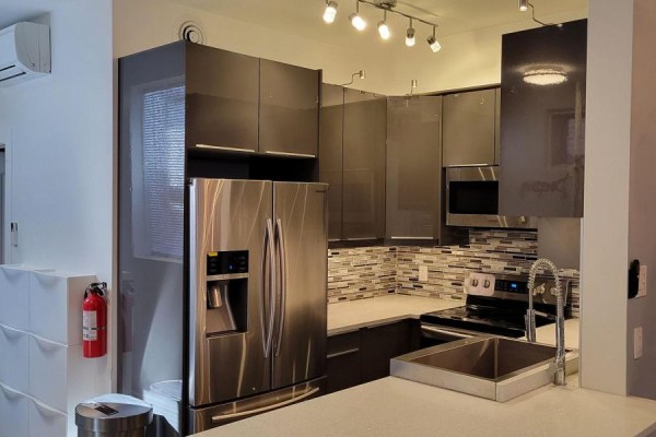 A modern kitchen has grey high-gloss cabinets, a stainless steel refrigerator, and a subway tile backsplash. - Unit B - 82 Third Avenue, Ottawa