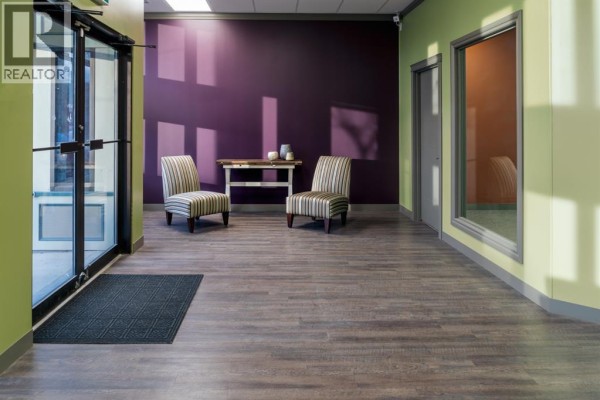 Reception area with glass double doors, two striped chairs, and a dark purple accent wall. - Unit D, 5051 50 Street, Camrose