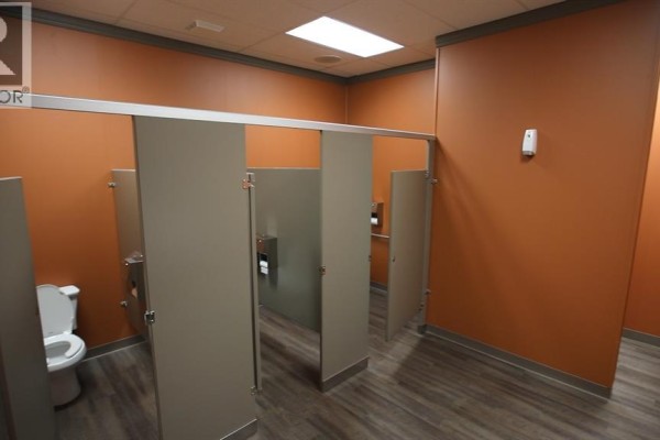 Restroom with three neutral-colored stalls and orange walls. - Unit D, 5051 50 Street, Camrose