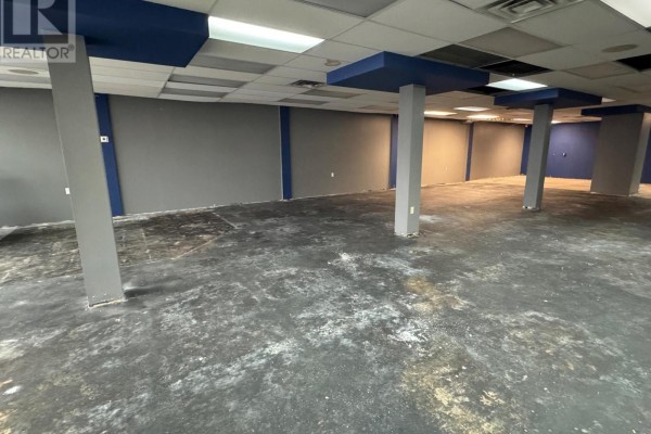 Empty commercial interior with grey walls, concrete floor, and ceiling light panels. - Unit J - 3505 Portage Road, Niagara Falls