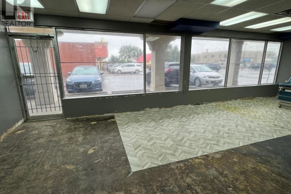 Storefront with large windows overlooking a parking lot, metal gate, and unfinished floor. - Unit J - 3505 Portage Road, Niagara Falls