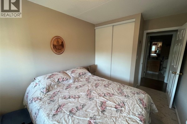 Bedroom with a double bed, floral comforter, and a closet with sliding doors. - Unit306 1 26th Street E, Prince Albert