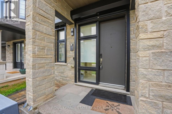Entrance to the modern house featuring a grey front door, stone cladding, and a small window. - Upper - 1192 Stag Hollow, Oakville