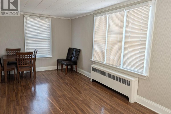 Dining area with wood table and chairs, wood-look laminate flooring, pale grey walls, and radiator under windows. - Upper - 12 East 24th Street, Hamilton