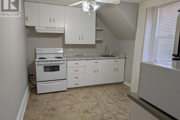 Small kitchen with white cabinets, white stove, marble-look counters, and beige speckled linoleum flooring. - Upper - 12 East 24th Street, Hamilton