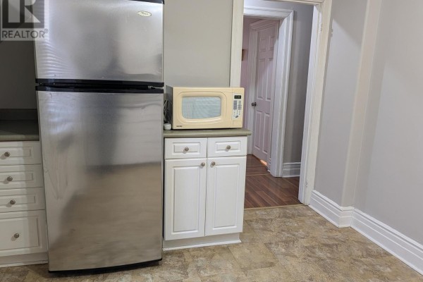 Kitchen corner with stainless steel refrigerator, microwave, white cabinets, and doorway to hallway with wood floors. - Upper - 12 East 24th Street, Hamilton