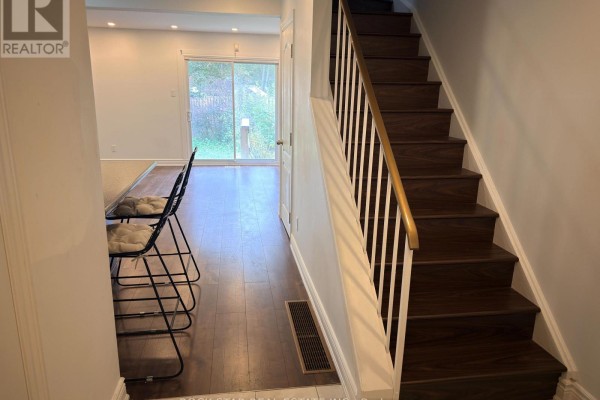 Interior view of a hallway with dark wood stairs and flooring, leading to a kitchen area and backyard. - Upper - 15 Hardcastle Court, Brampton