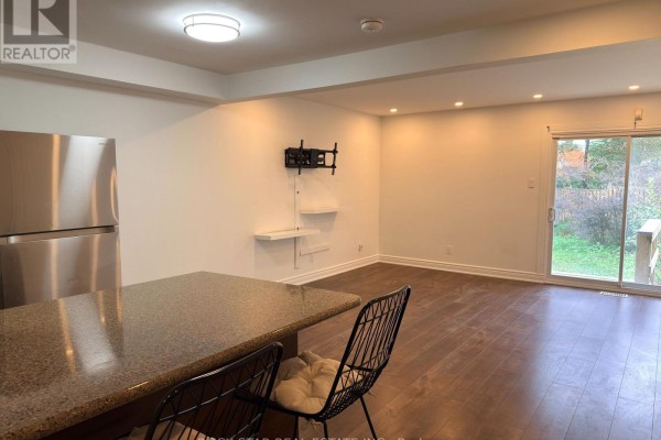 View of an open living area with dark wood floors, kitchen counter, and sliding glass doors to the backyard. - Upper - 15 Hardcastle Court, Brampton