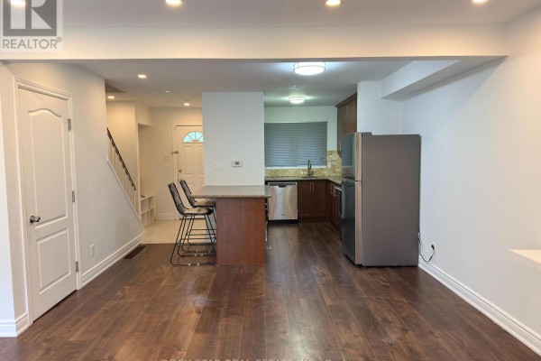 View of an open concept living space with a kitchen island, dark wood cabinets, and hallway leading to front entrance. - Upper - 15 Hardcastle Court, Brampton