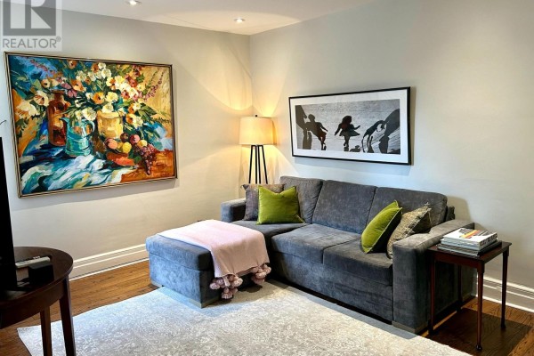 Living room with a grey sectional sofa, decorative pillows, and artwork on light grey walls. - Upper - 18 Pape Avenue, Toronto