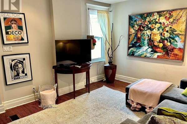 Living room featuring a television, a round wooden table, and colorful artwork on beige walls. - Upper - 18 Pape Avenue, Toronto