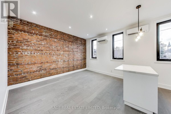 Living area with exposed brick wall, grey wood floors, white kitchen island, and mini-split AC. - Upper - 2551 Yonge Street, Toronto
