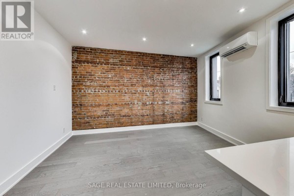 Living space featuring a red brick accent wall, grey hardwood floors, and a modern kitchen island. - Upper - 2551 Yonge Street, Toronto