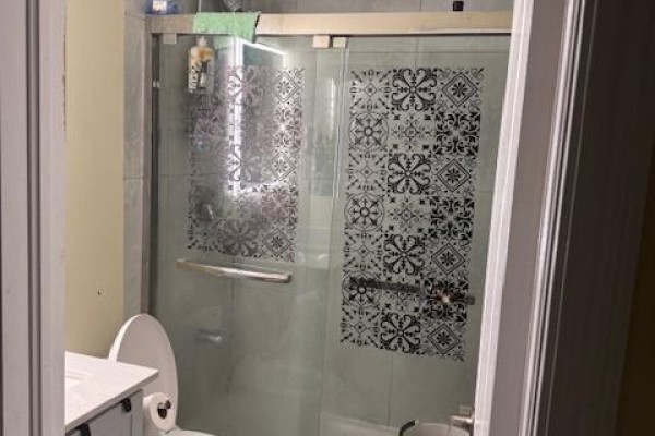Bathroom with a white toilet and a glass-enclosed shower featuring decorative patterned tiles. - Upper - 3038 Coral Drive, Mississauga