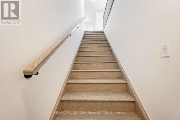 Wooden staircase with a light oak finish and black metal railing ascending indoors. - Upper - 34 Thornbird Crescent, Brampton