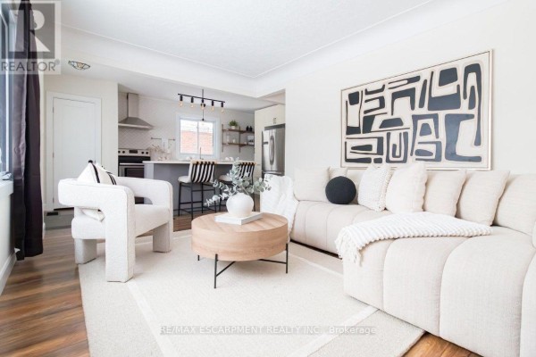 Living room with a large sectional sofa, accent chair, coffee table, and kitchen island. - Upper - 374 East 16th Street, Hamilton