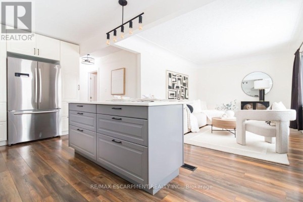 Kitchen with gray island, stainless steel refrigerator, and open-concept living area. - Upper - 374 East 16th Street, Hamilton