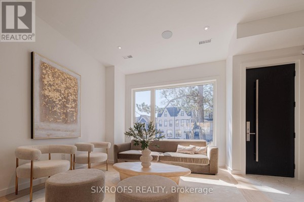 Living room with sofa, armchairs, oval coffee table, and modern artwork, facing a large window. - Upper - 40 Morningside Avenue, Toronto