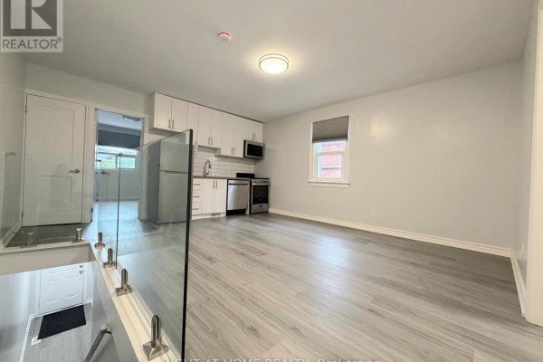 Open concept living area with light grey walls, grey flooring, white cabinetry, and stainless steel appliances. - Upper - 408 Strathmore Boulevard, Toronto