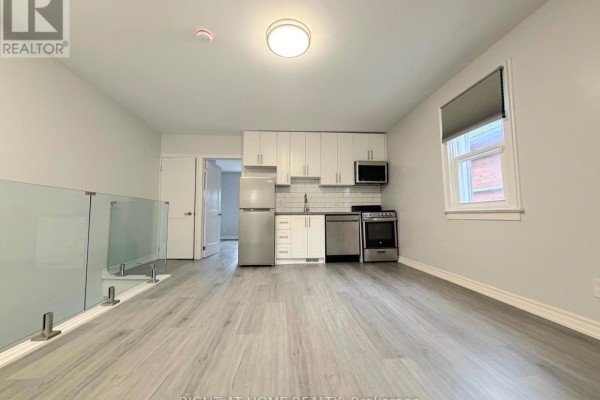 Combined kitchen and living area with white cabinets, stainless steel appliances, grey flooring, and glass railing. - Upper - 408 Strathmore Boulevard, Toronto