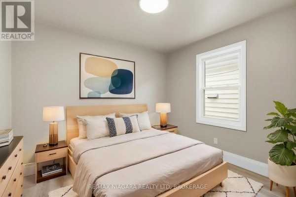 Bedroom with a queen-size bed, nightstands, and a television, with a window facing the side. - Upper - 422 Brunswick Street, Hamilton