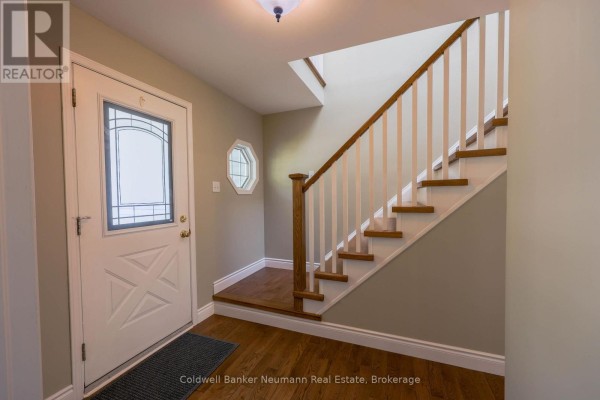 Interior entryway with a white front door, hardwood floors, a white staircase with wooden railing, and an octagonal window. - Upper - 44 Tanager Drive, Guelph