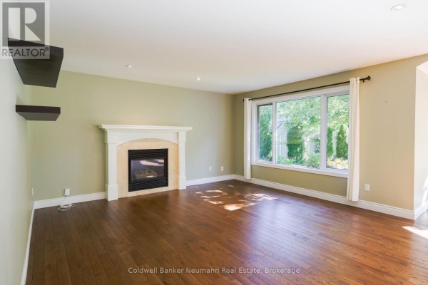 Living room with hardwood floors, a marble-surround fireplace with a white mantle, and a large window overlooking greenery. - Upper - 44 Tanager Drive, Guelph