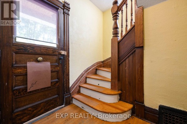 Interior view of a curved wooden staircase with white risers and yellow walls near the entrance. - Upper - 52 First Street, Orangeville