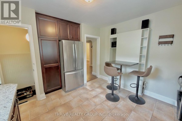 Kitchen with stainless steel refrigerator, dark cabinets, and a view into a hallway. - Upper - 538 Quebec Street, London East
