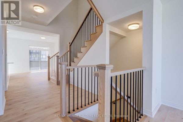 Interior hallway with a prominent wooden staircase featuring black spindles and light wood flooring. - Upper - 6 Thornbird Crescent, Brampton