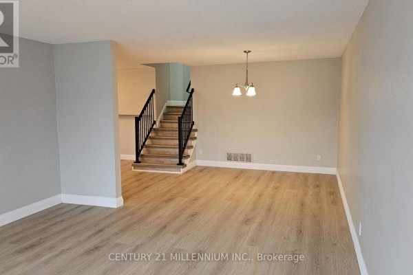 Living room with light wood laminate flooring, grey walls, and stairs in background. - Upper - 67 Simmons Boulevard, Brampton