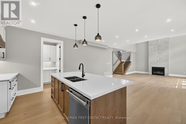 Island kitchen with pendant lights, adjacent to a living area with a fireplace and staircase. - Upper - 929 7th Line, Innisfil