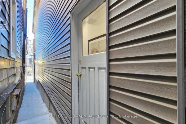 Narrow side alleyway with a grey vinyl-sided building and a white door with brass knob. - Upper 1 - 1930 Queen Street E, Toronto