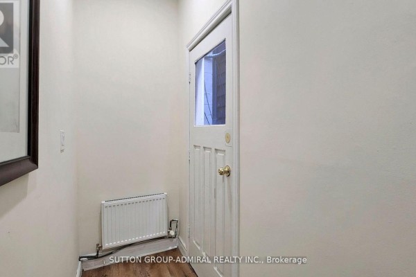 Interior hallway with a white door, glass window, brass knob, and a white baseboard heater. - Upper 1 - 1930 Queen Street E, Toronto
