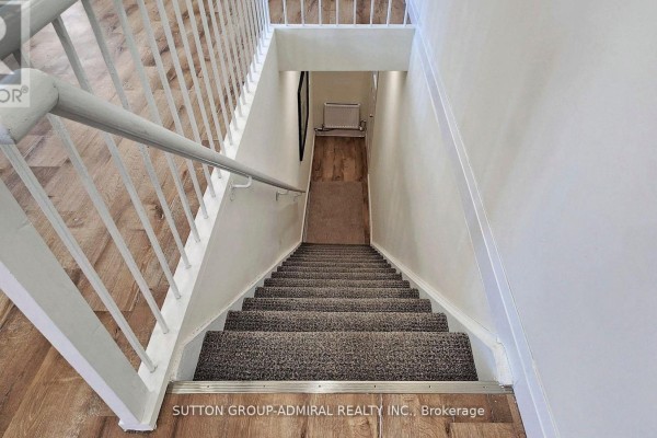 Top-down view of a carpeted staircase with grey and white railings and wood-look flooring. - Upper 1 - 1930 Queen Street E, Toronto
