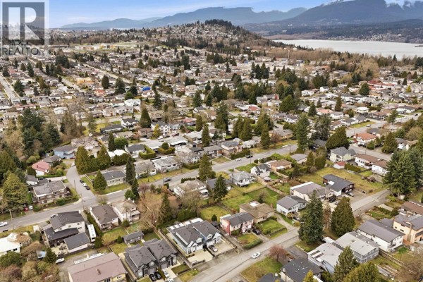 Aerial view of a suburban neighborhood with houses, streets, trees, and distant mountains. - Upper 1106 Duthie Avenue, Burnaby