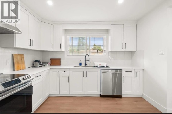 Corner kitchen with white shaker cabinets, quartz countertops, stainless steel appliances, and wood flooring. - Upper 1106 Duthie Avenue, Burnaby