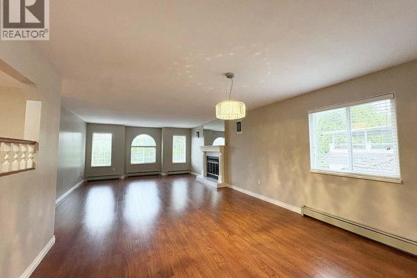 Spacious living room with fireplace, windows, and hardwood flooring. - Upper 5225 Canada Way, Burnaby