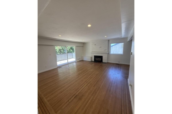 Living room with hardwood floors, white brick fireplace, large sliding glass doors, and view to balcony. - Upper 9655 Townline Diversion, Surrey