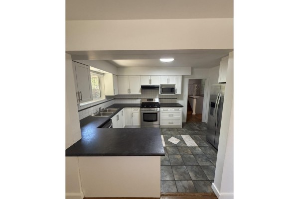 White kitchen with dark countertops, stainless steel appliances, and a view into a hallway and bathroom. - Upper 9655 Townline Diversion, Surrey