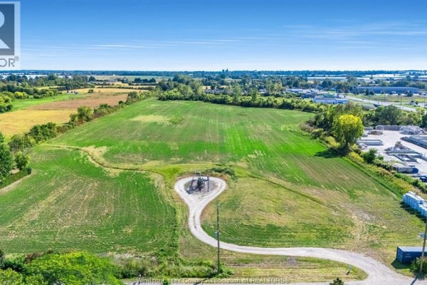 Aerial view of a large, green, undeveloped lot with a winding asphalt driveway and a metal structure. - V/l Mersea Road 5, Leamington