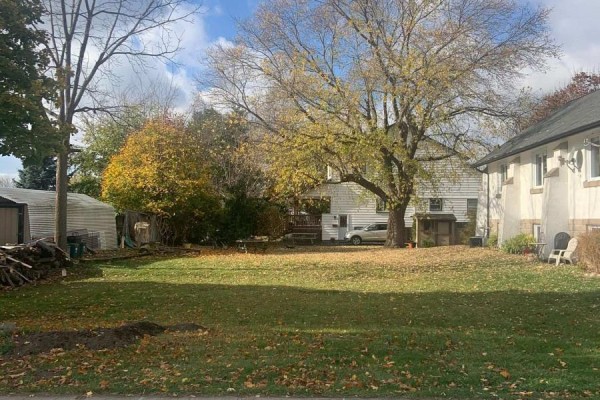Backyard view of a grassy lot with a large tree and a white house with visible sheds. - W/s Fielden Avenue, Port Colborne